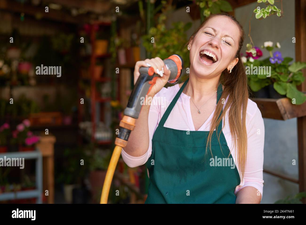 Young gardener sings loudly and exuberantly with hose as a microphone in the flower shop Stock Photo