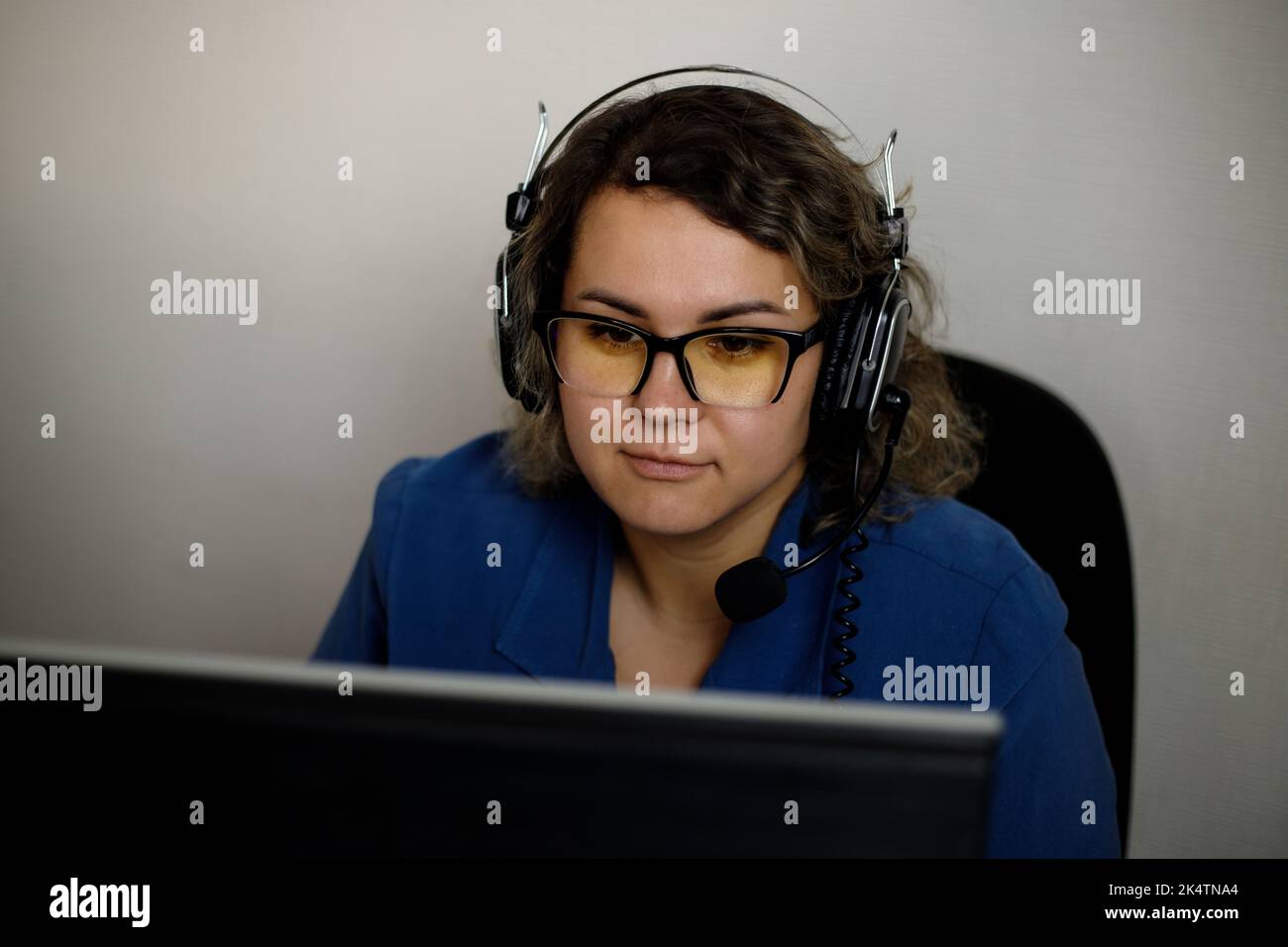 A serious call center operator is talking to a client while looking at a computer screen in close-up. A telemarketer, a telemarketing agent, makes a c Stock Photo