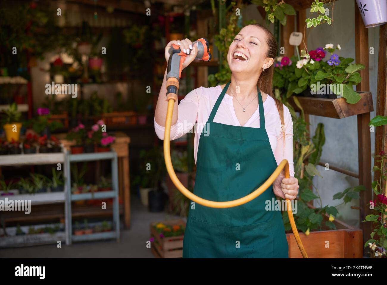 Young florist with garden hose sings out of high spirits and joie de vivre in the flower shop Stock Photo