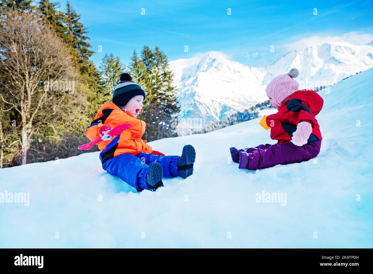 Little boy and girl sit in snow throw snowballs at each other Stock Photo