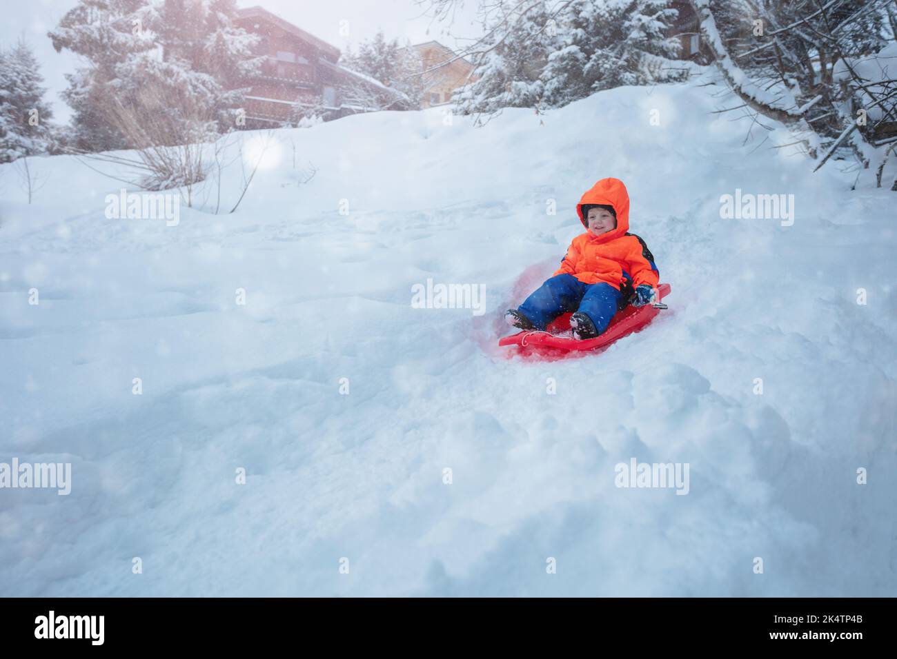 Cute boy in orange ski sport outfit go downhill on the sledge Stock Photo