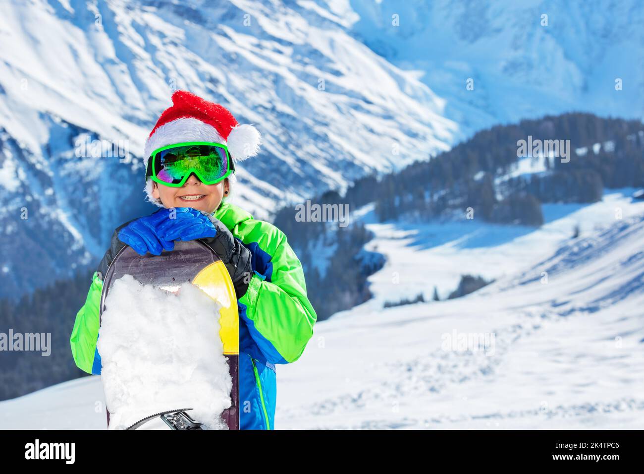 Close portrait of boy in Santa hat and googles with snowboard Stock Photo