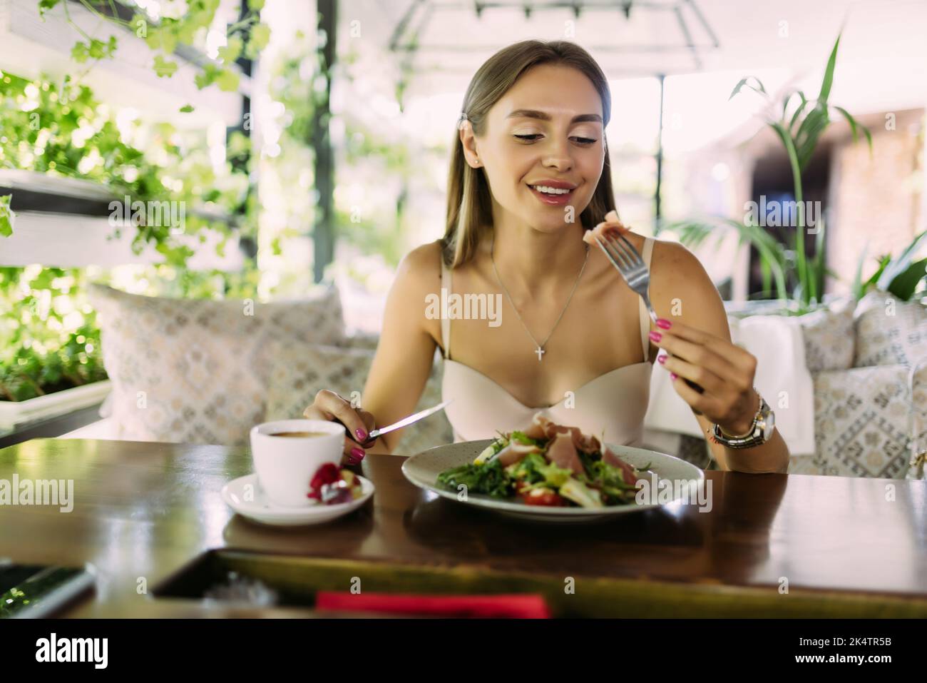 Young woman eating healthy food sitting in the beautiful interior with green flowers on the background Stock Photo
