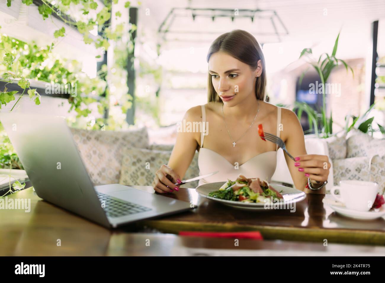 Pensive young business woman having her lunch at the roof top restaurants open air light terrace looking at the screen of her laptop Stock Photo