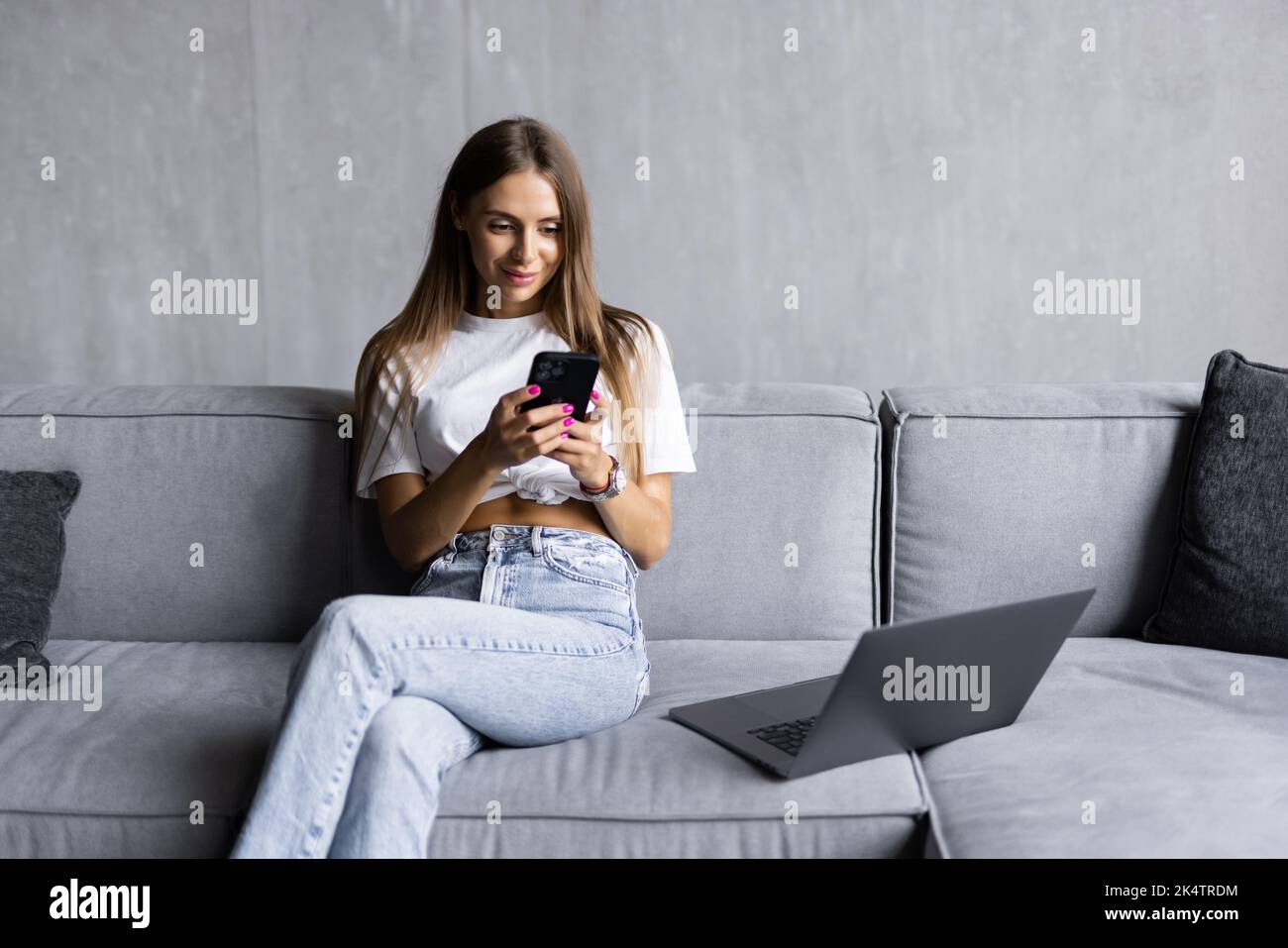 Beautiful smiling young brunette woman relaxing on a couch at home, using mobile phone Stock Photo