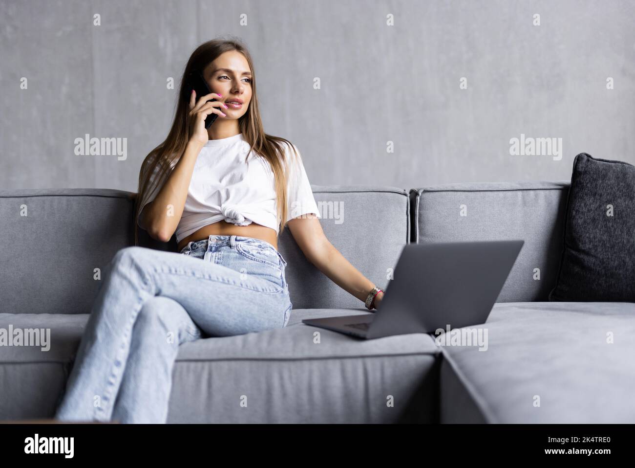 Casual young woman using laptop and cellphone on sofa at home Stock Photo