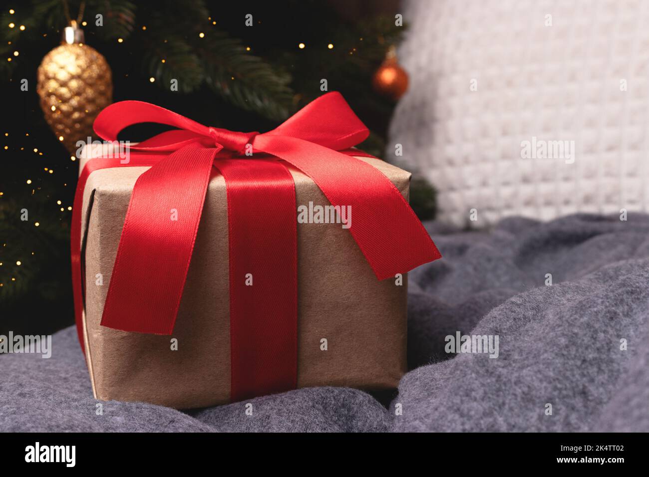 Gift box with red ribbon on a couch in front of decorated fir tree ...