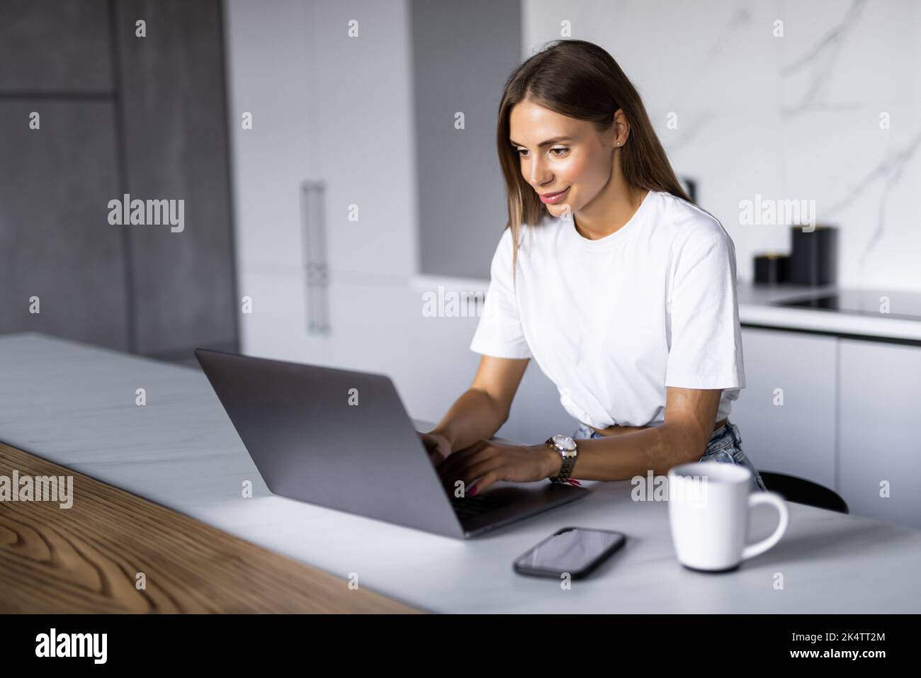 Shot of thoughtful young woman looking her laptop while holding a cup of coffee in the kitchen at home. Stock Photo