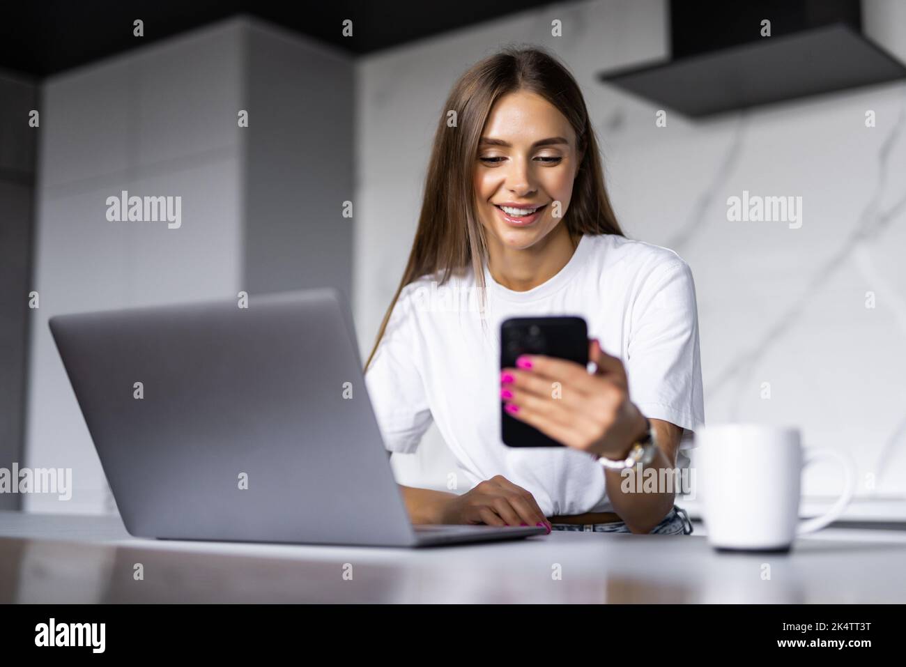 Young woman use a laptop to work in the kitchen use the phone Stock Photo