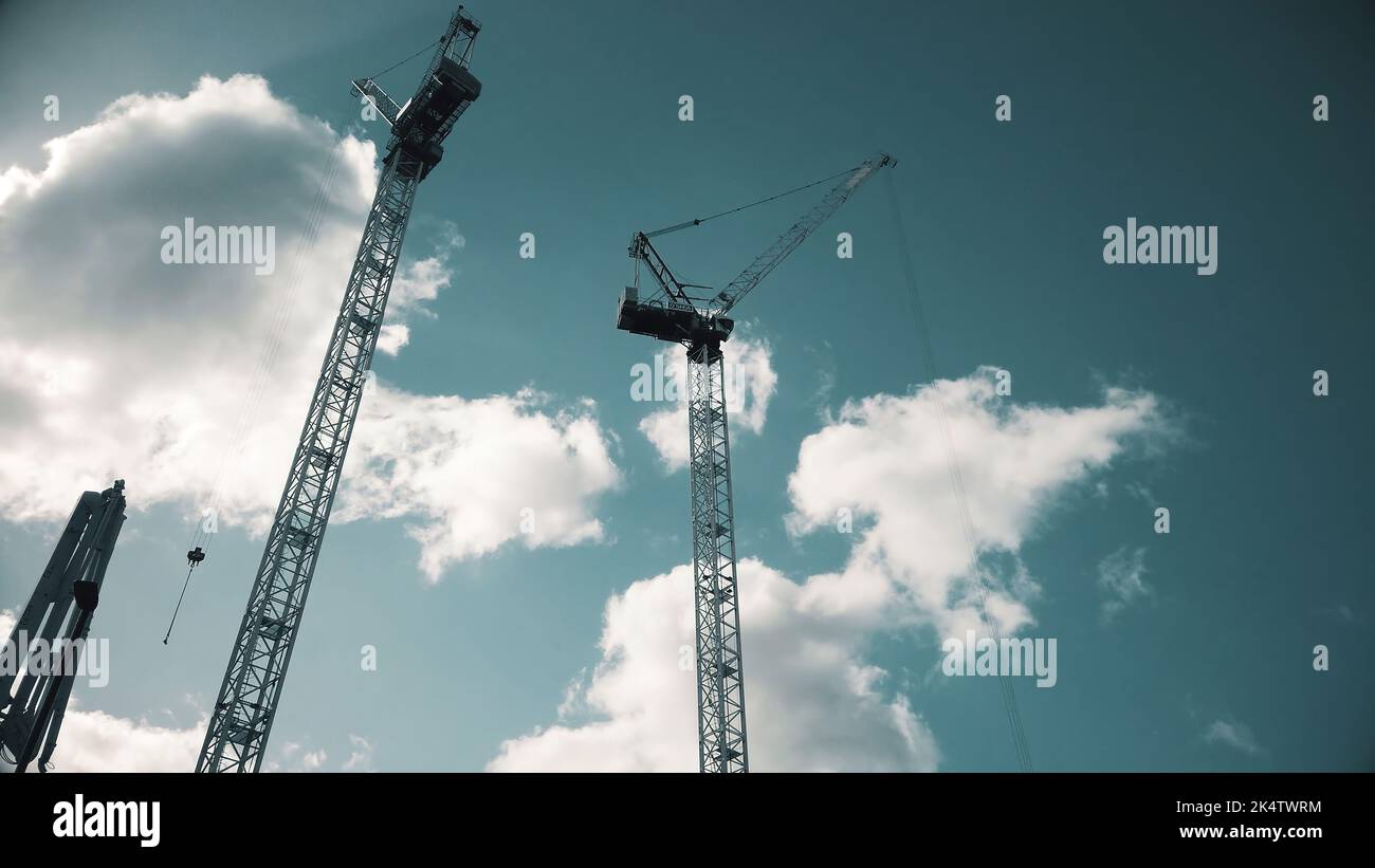 A low angle shot of tall crane towers at a construction site on blue ...