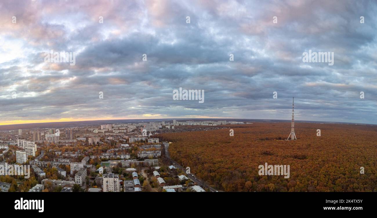 Aerial sunset panorama view on autumn city with telecommunication tower in forest near residential district with scenic cloudy sky. Kharkiv, Ukraine Stock Photo