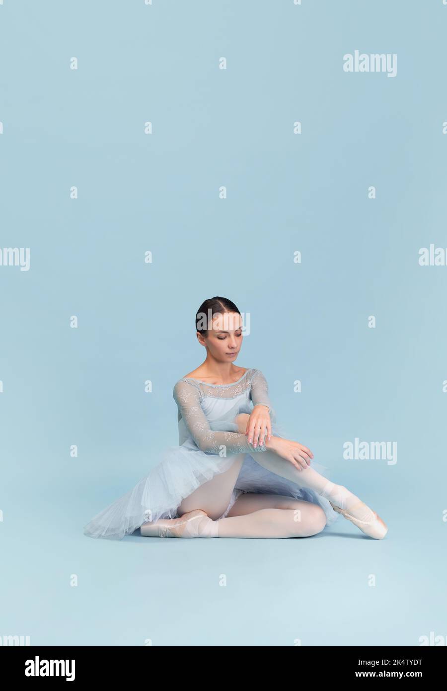 Portrait of tender young ballerina dancing, performing isolated over blue studio background