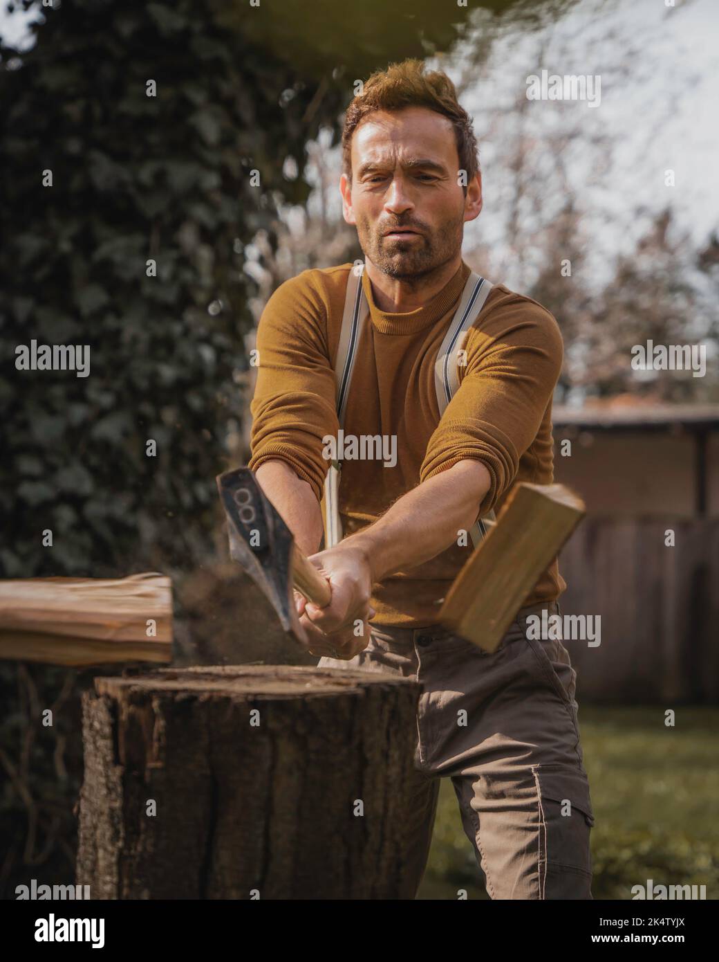 Man in brown clothes is chopping wood with an axe Stock Photo