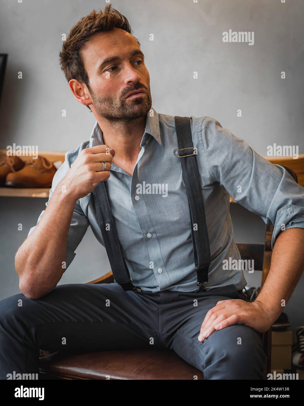 male model in gray vintage clothing sitting an a chair posing in a leather shop 2K4W13R