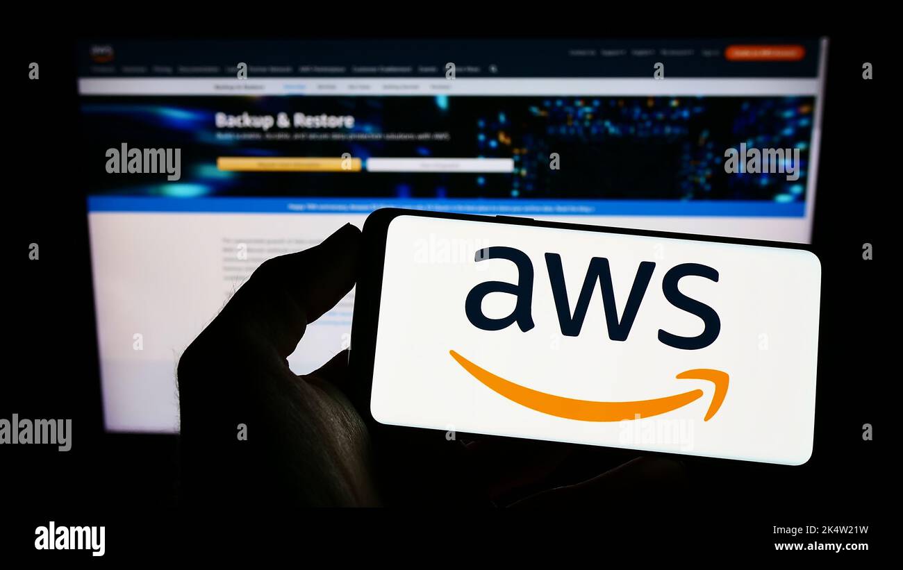Person holding cellphone with logo of American cloud company Amazon Web Services Inc. (AWS) on screen in front of webpage. Focus on phone display. Stock Photo