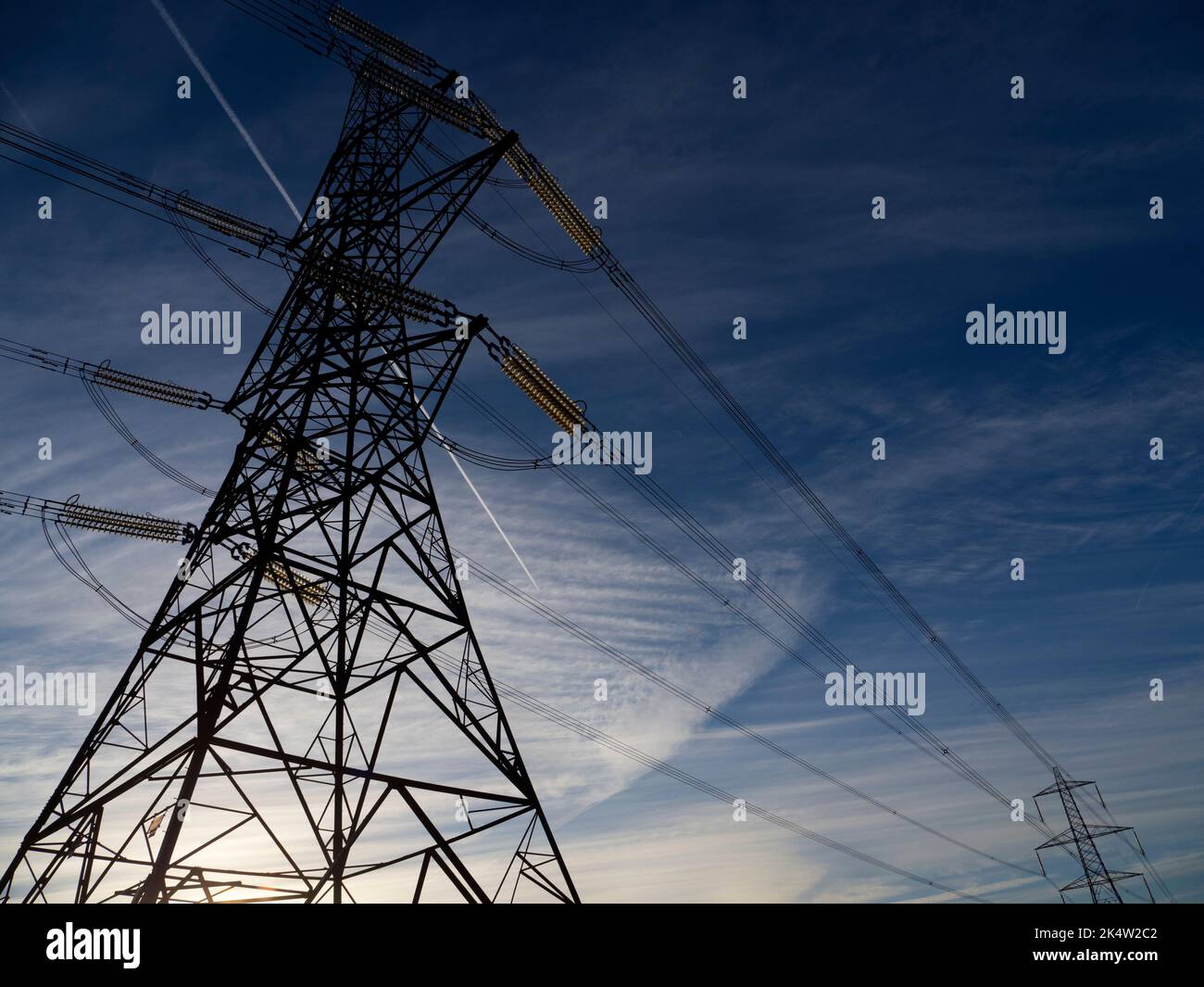 I love electricity pylons; I find their abstract, gaunt shapes endlessly fascinating. Here we see two giant pylons in a field by the Thames at Kenning Stock Photo
