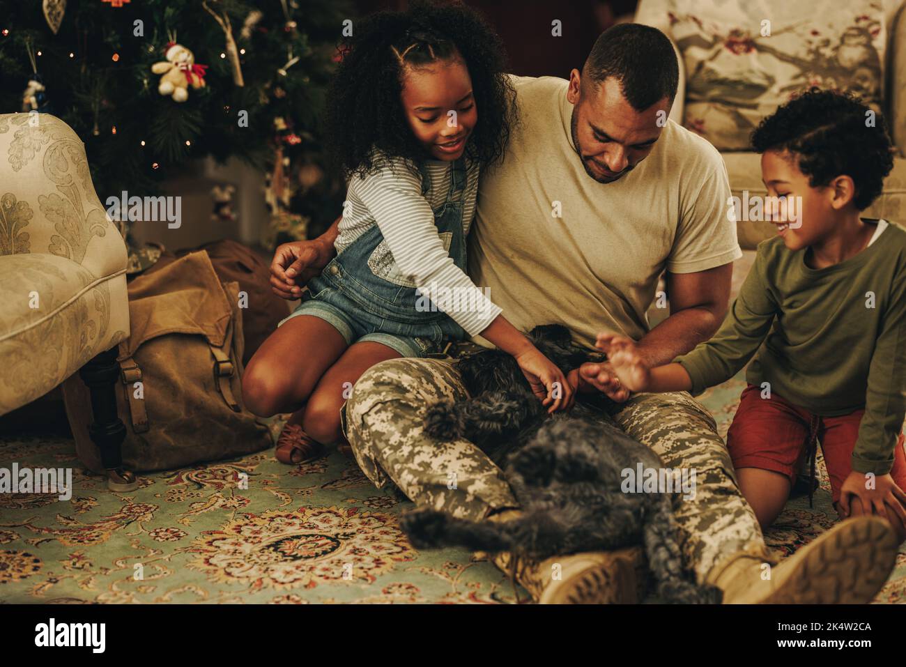 Happy military family playing with their cat at Christmas. Military dad reuniting with his children at home. Soldier spending quality time with his fa Stock Photo
