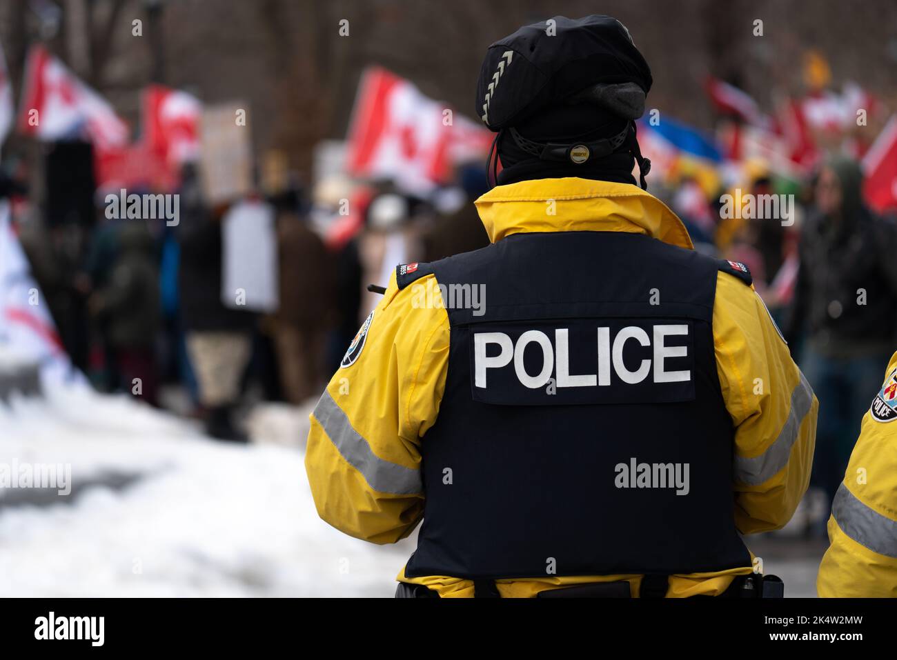 Police officer wearing a black vest and a yellow jacket while on duty patrolling the streets of Toronto at Queen's Park anti-vaccination mandate rally. Stock Photo