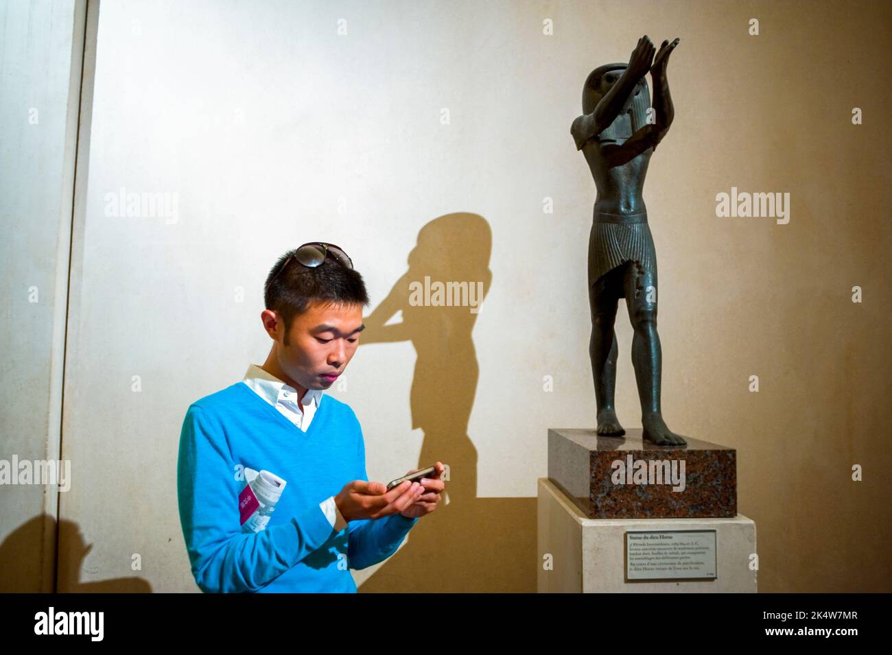 Paris, France, Young Chinese Tourist Sending Text Message on Smart Phone, Iphone, in Egyptian Antiquities Art Gallery of the Louvre Museum, 'Statue of Horus god' Stock Photo