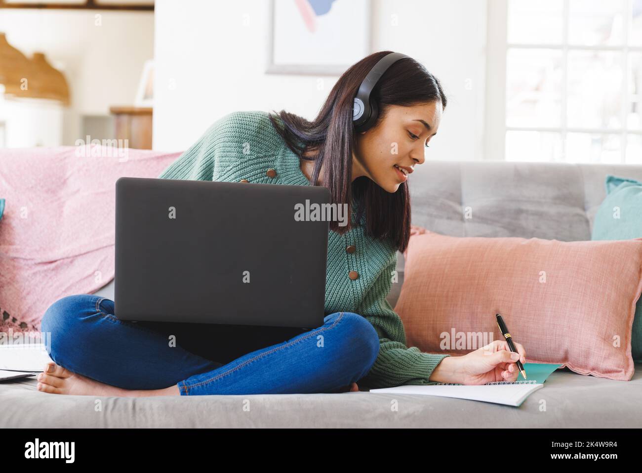 Happy biracial woman sitting on sofa in living room, using laptop and ...