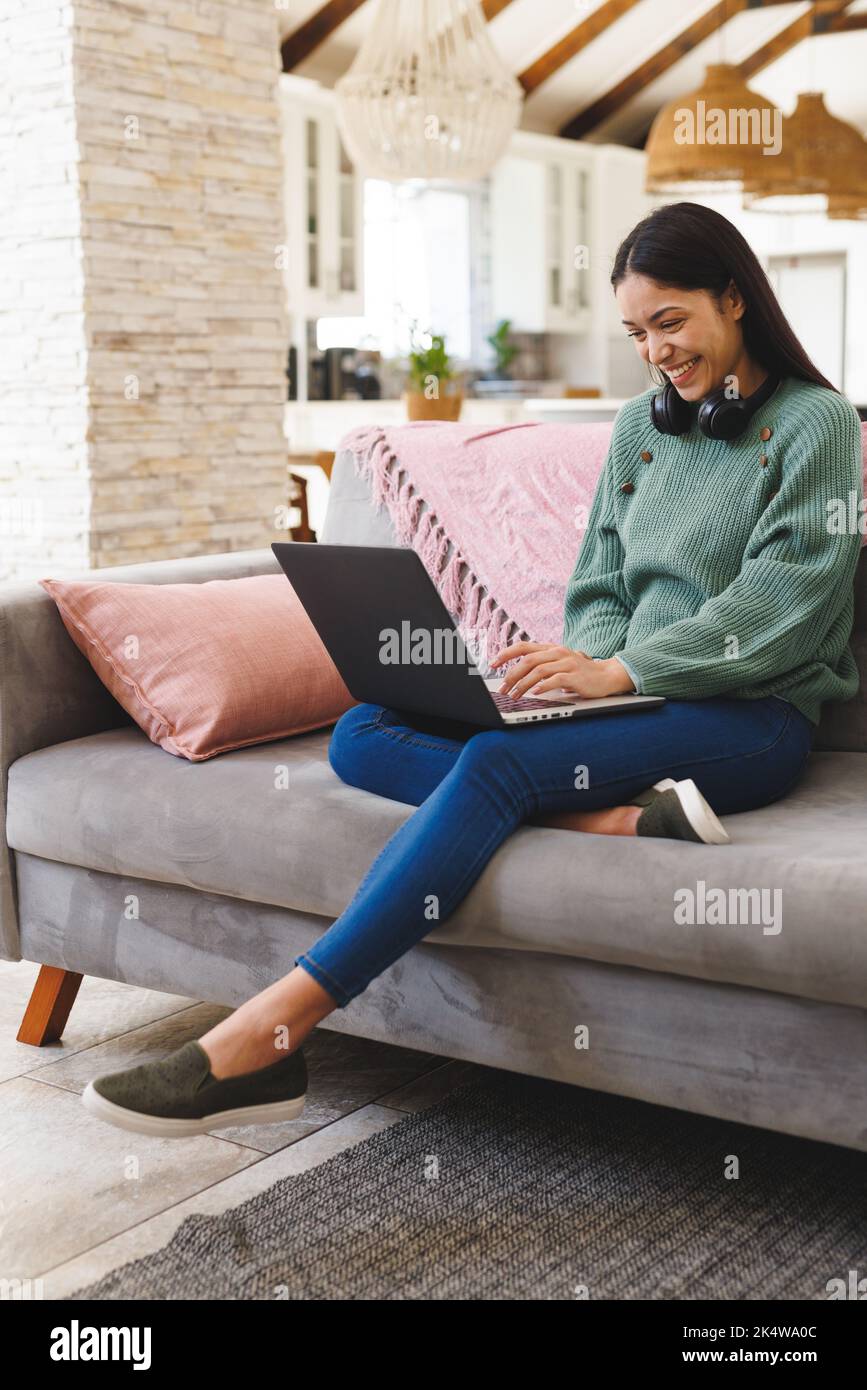 Happy biracial woman sitting on sofa in living room, using laptop Stock ...