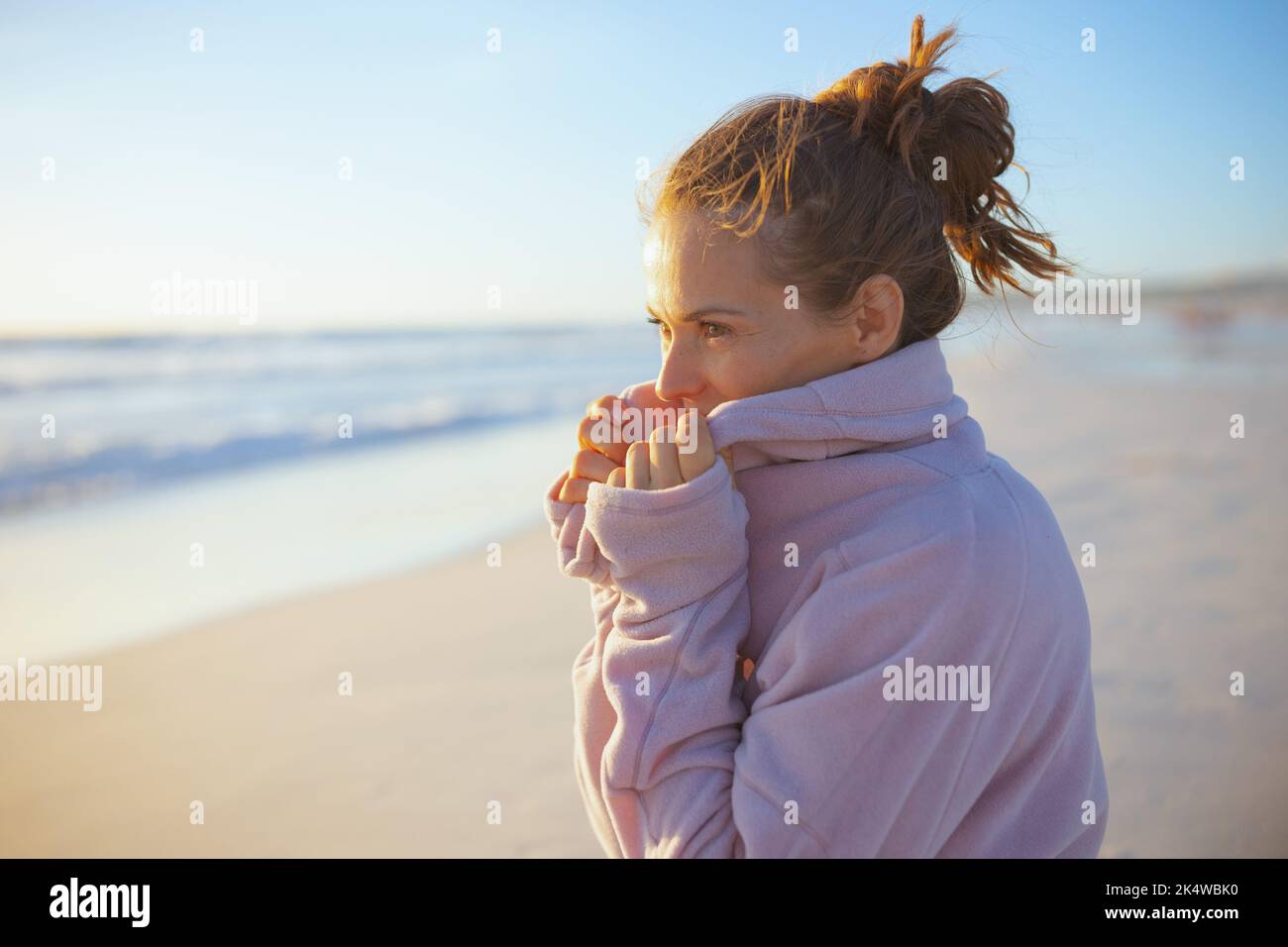 elegant 40 years old woman in cosy sweater at the beach in the evening relaxing. Stock Photo