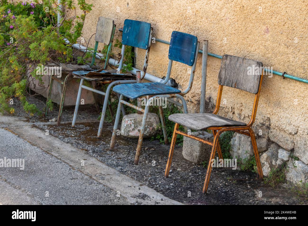 four old chairs left outside in the elements to rust away, 4 chairs outside of a rural building in greece, chairs rusting in the rain left outside. Stock Photo