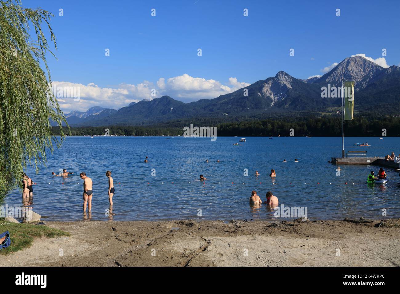 CARINTHIA, AUSTRIA - AUGUST 10, 2022: Tourists enjoy the summer at Lake Faak (Faaker See) with view of Karawanks mountain range (Karawanken) in Austri Stock Photo