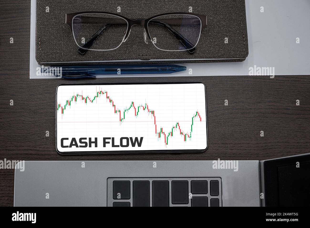 Cash flow text in phone. Top view of chart in the phone on the table near laptop, notepad, and glasses. Stock Photo