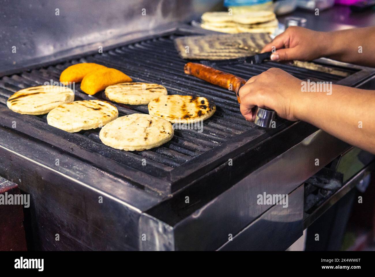 Close-up of a woman's hands cutting a chorizo and preparing Colombian arepas and empanadas on a charcoal grill Stock Photo