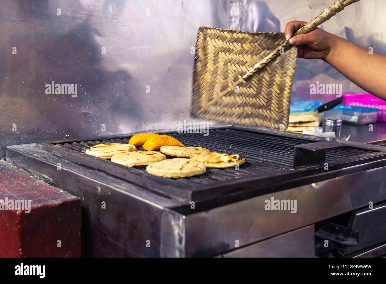 Close-up of a woman's hand fanning the charcoal from the grill to prepare Colombian empanadas and arepas with a fan Stock Photo
