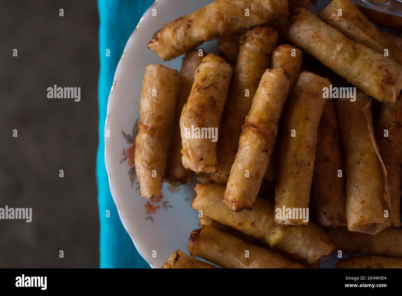 Flat lay shot of delicious and crunchy vegetable spring rolls AKA Filipino vegetarian lumpia on white plate on blue tablecloth. Selective focus. Stock Photo
