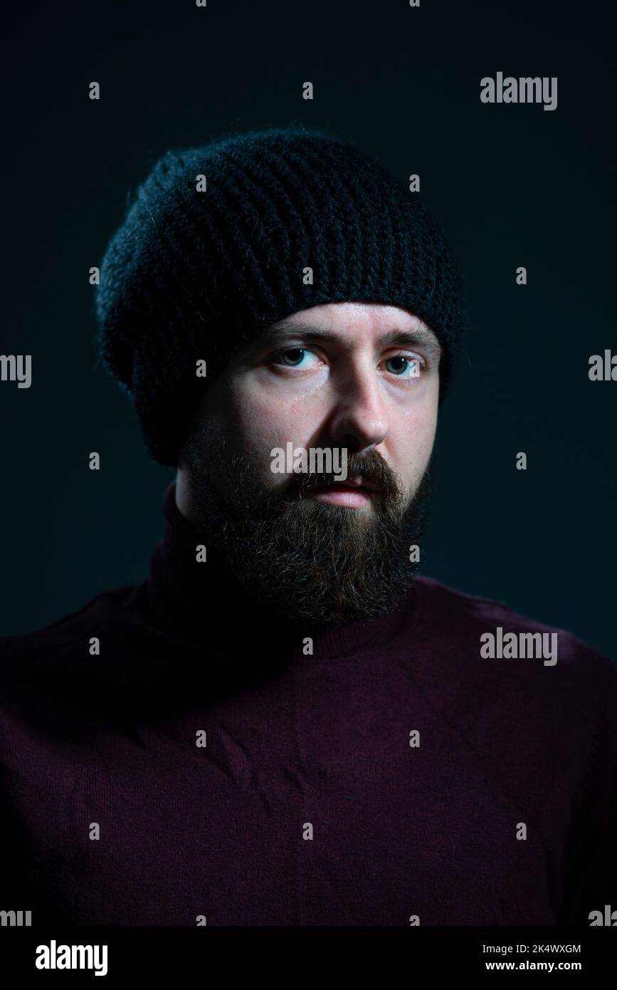 dramatic portrait of millennial in black knitted hat and sweater on dark background. Stock Photo