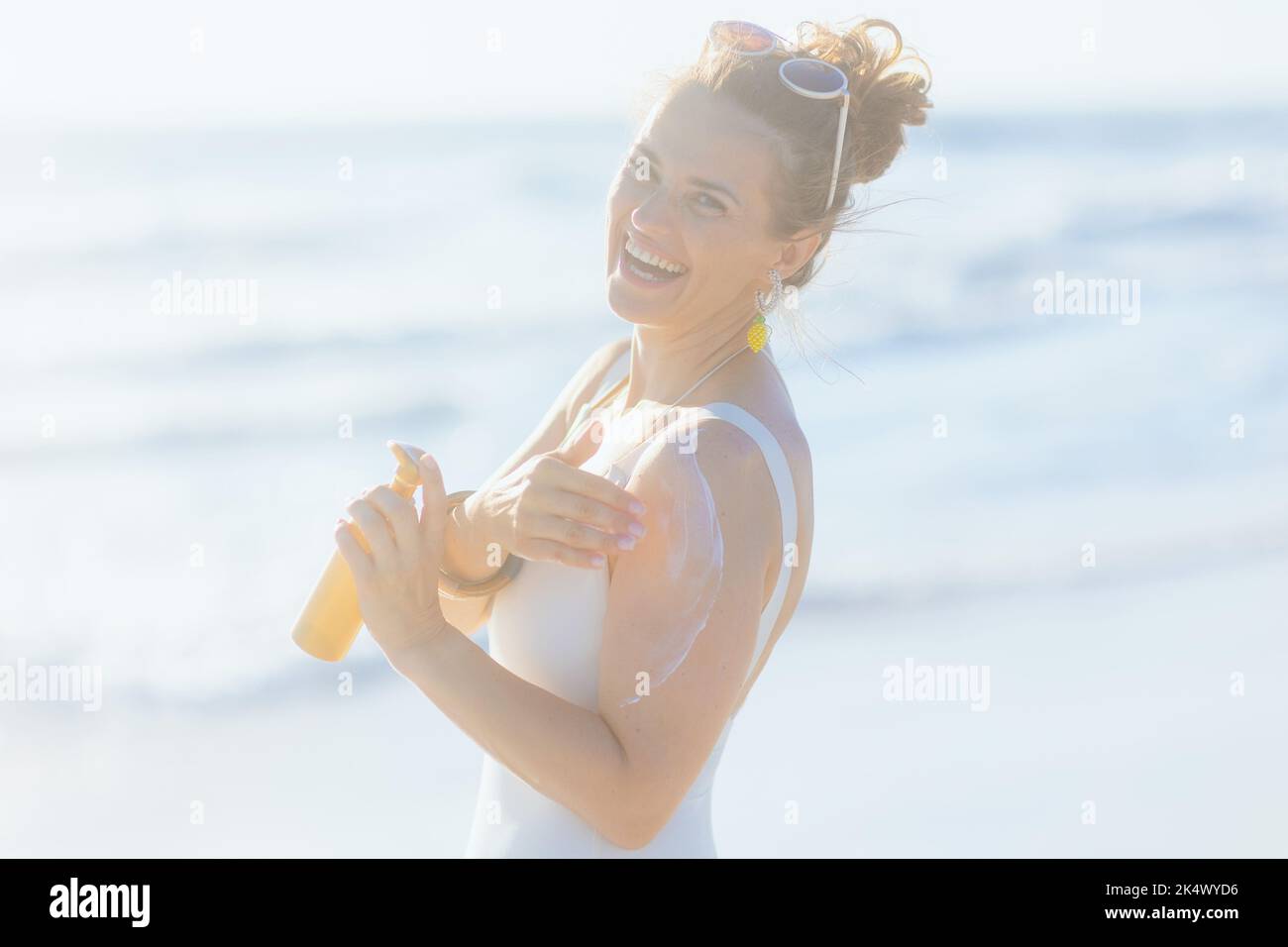 Portrait of happy elegant woman in white beachwear with sunscreen at the beach. Stock Photo