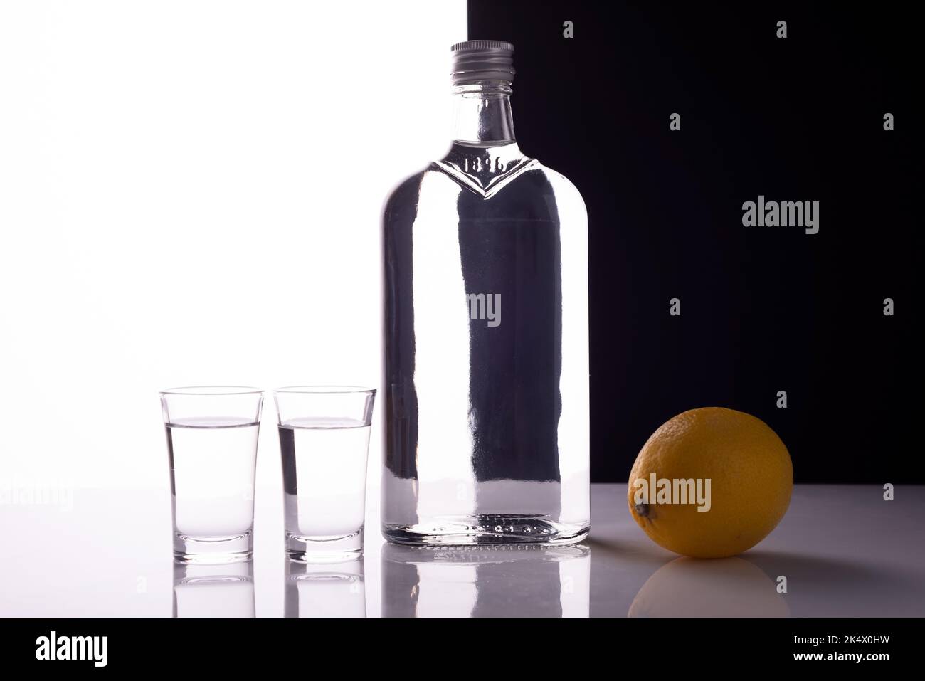 gin bottle with shot glasses on black and white background alcoholic drink with lemon. Stock Photo