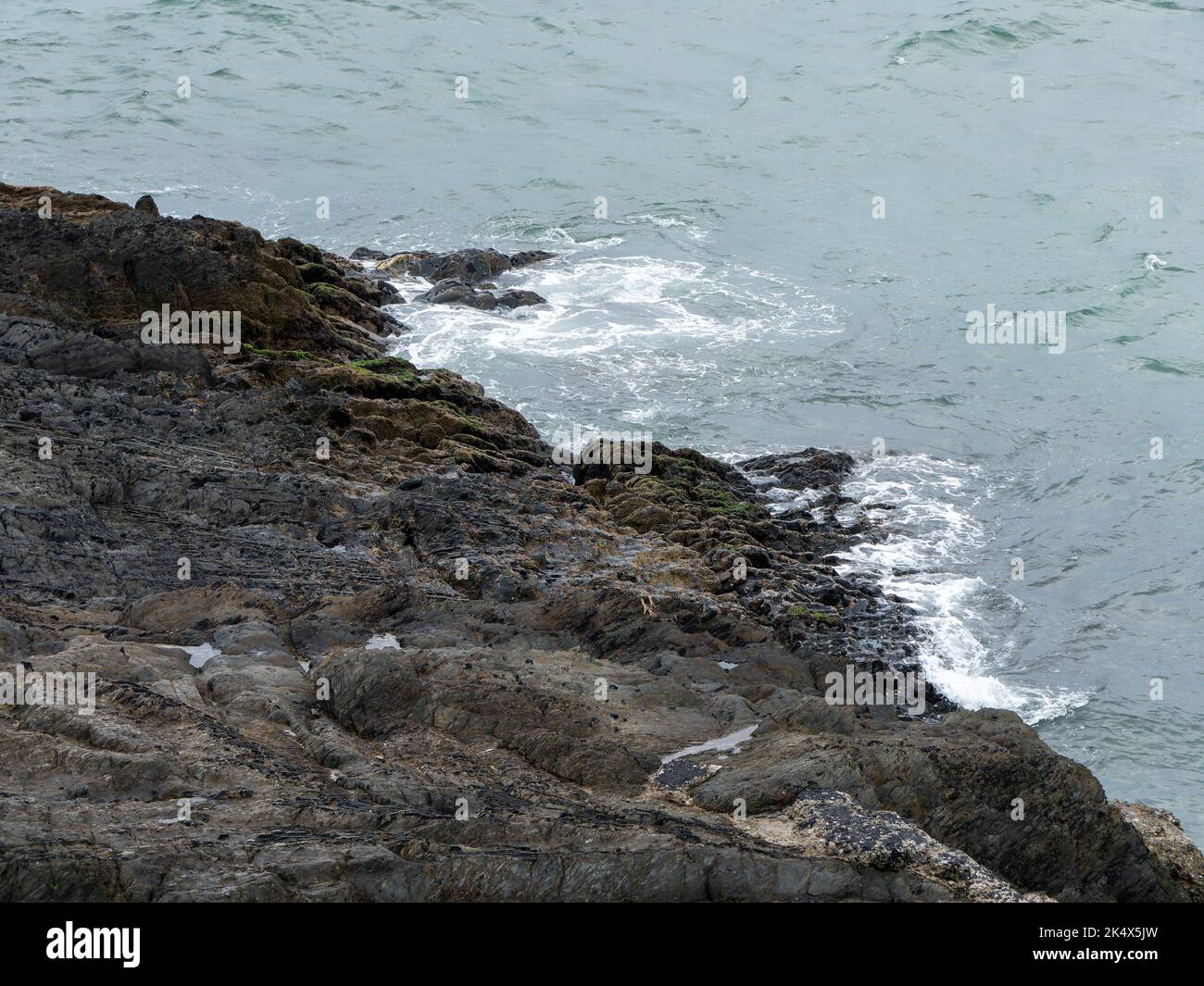 Cold sea water and coastal rocks. Cloudy weather on the coast. Surf and white sea foam, rock formation beside body of water. Stock Photo