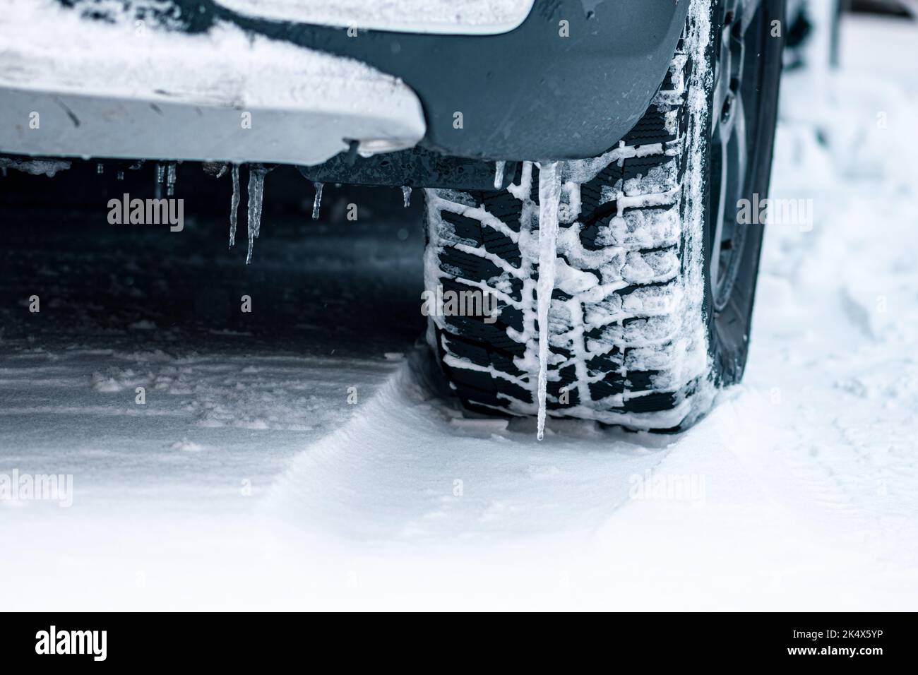 Close up winter tire of a car on the road covered by snow and ice driving in extreme cold