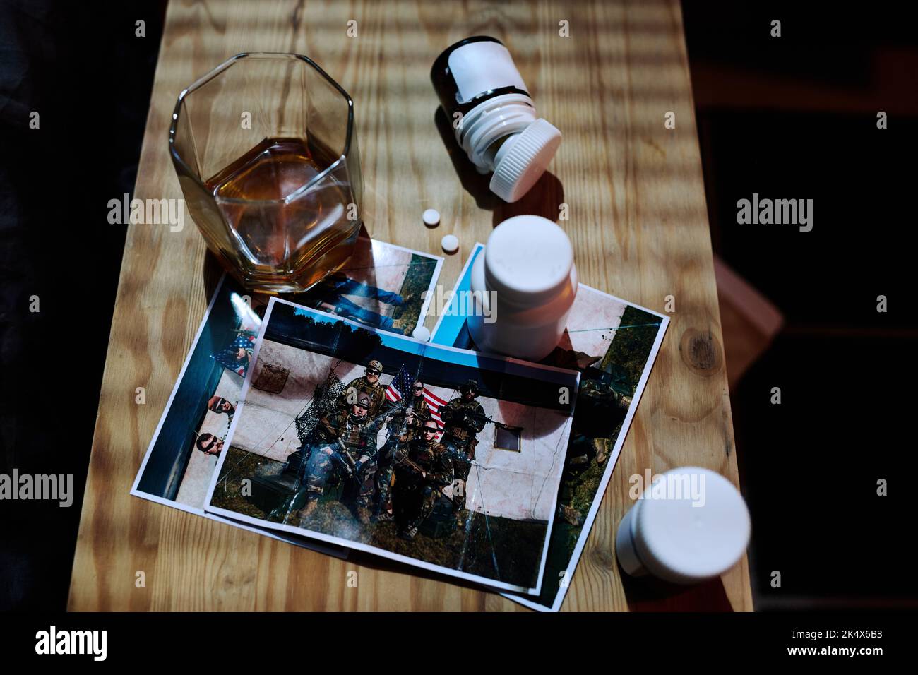 Above angle of wooden night table with bottles with various pills, photos of army friends and glass of whisky standing by bed Stock Photo