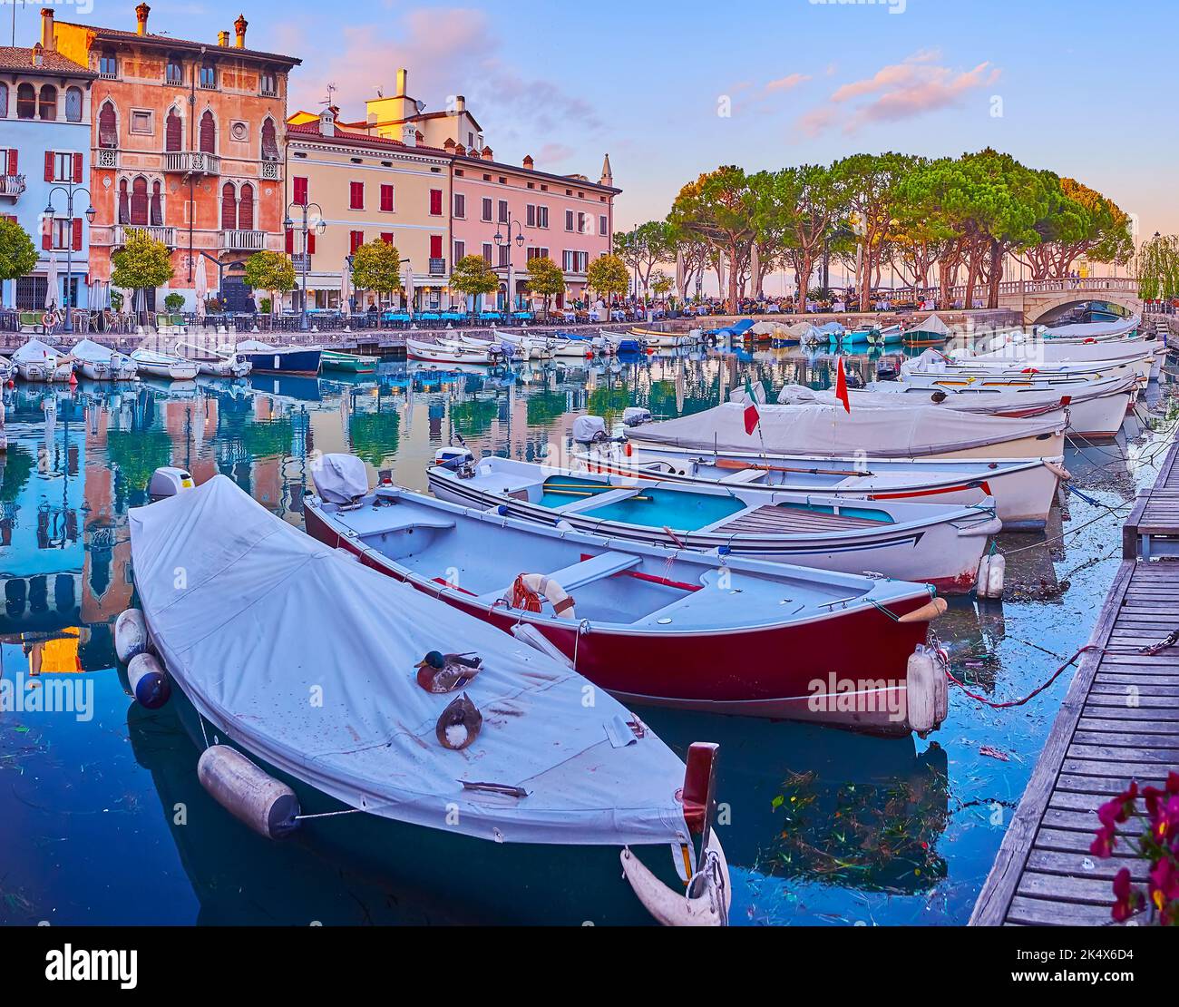 Enjoy the walk on sunset in Porto Vecchio (Old Port) with a view on small fishing boats, lush pines and colored houses, Desenzano del Garda, Lake Gard Stock Photo