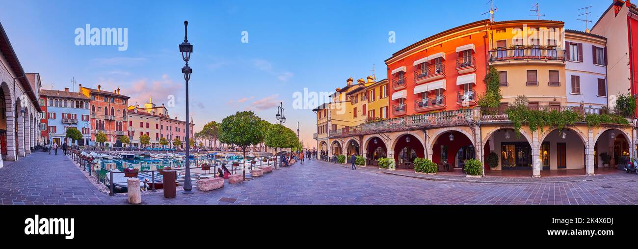 Panorama of the old housing, outdoor cafes, boats moored in Porto Vecchio (Old Port) at sunset, Desenzano del Garda, Italy Stock Photo
