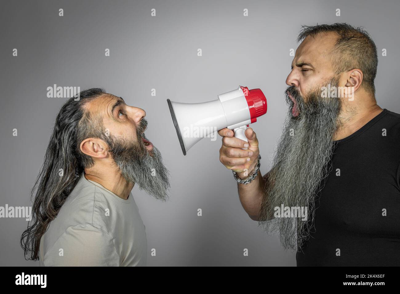 man yells with megaphone to another man with long hair Stock Photo