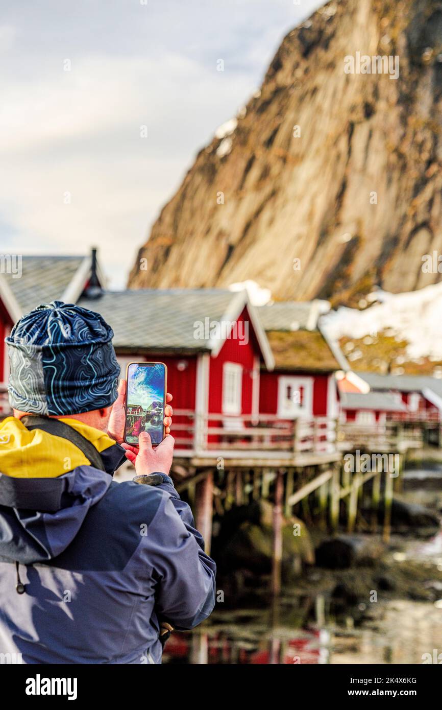Rear view of tourist photographing red Rorbu cabins in the fishing village of Reine, Lofoten Islands, Nordland county, Norway Stock Photo