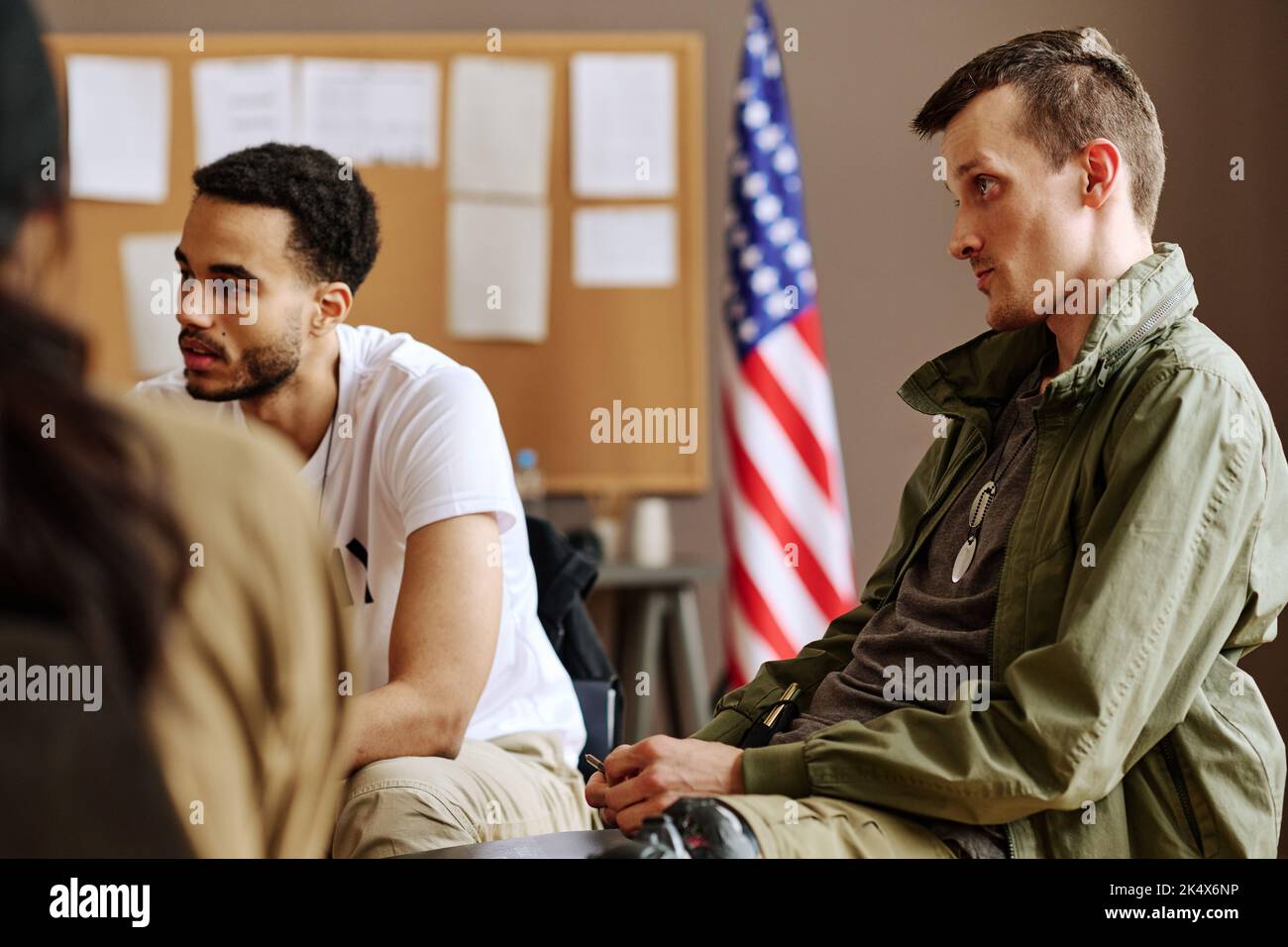 Young man looking at psychotherapist and listening to his advice while sitting among attendants of psychological session Stock Photo
