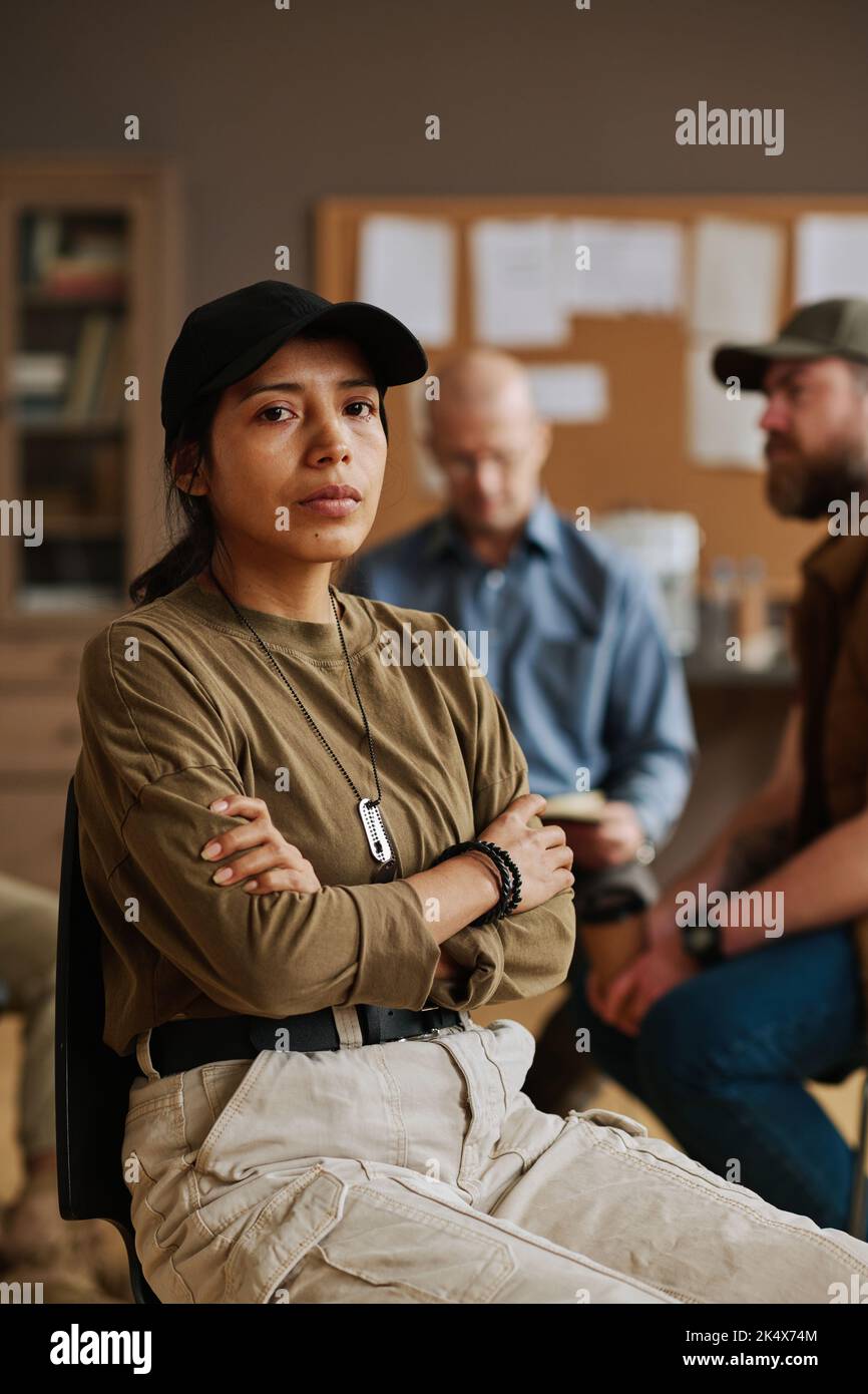 Young depressed Hispanic woman with military dog tag on ball chain hanging on her neck looking at camera during psychological session Stock Photo