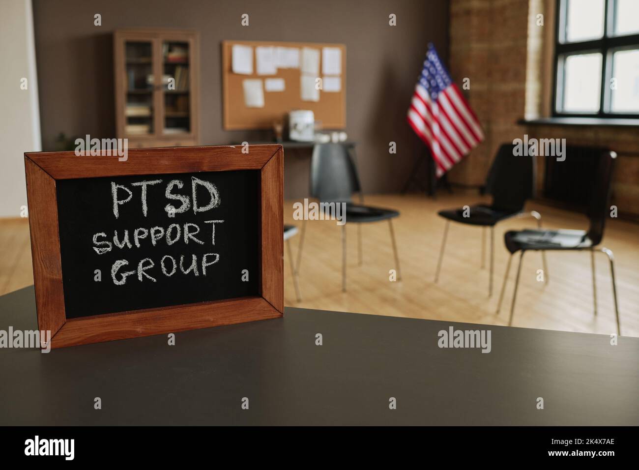 Small chalkboard with notice about PTSD support group on table standing against circle of several chairs for attendants in studio Stock Photo