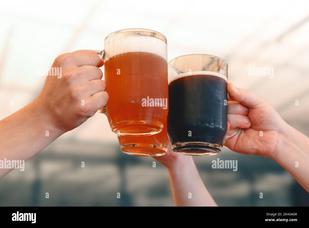 Male hands holding three glass mugs of light and dark draft beer. Beer toast, cheers Stock Photo