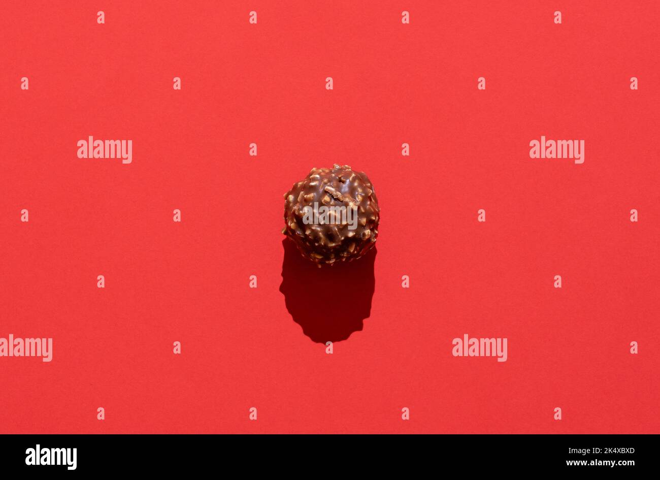 Directly above view with one chocolate candy on a red background. Delicious hazelnut and chocolate truffle isolated on a colorful table. Stock Photo