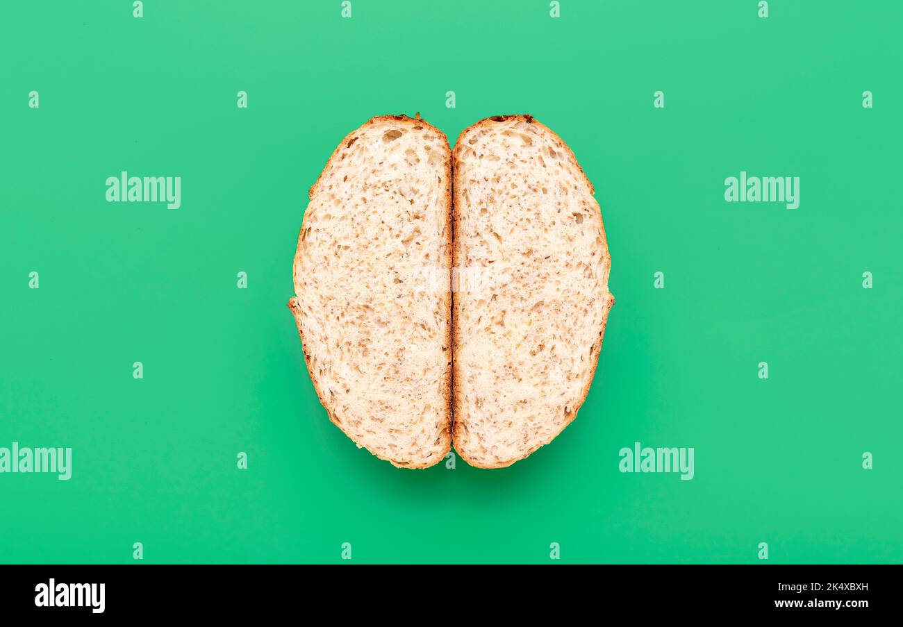 Top view with a loaf of bread sliced in half, minimalist on a green table. Cross section with a freshly baked white bread with sesame seeds. Stock Photo