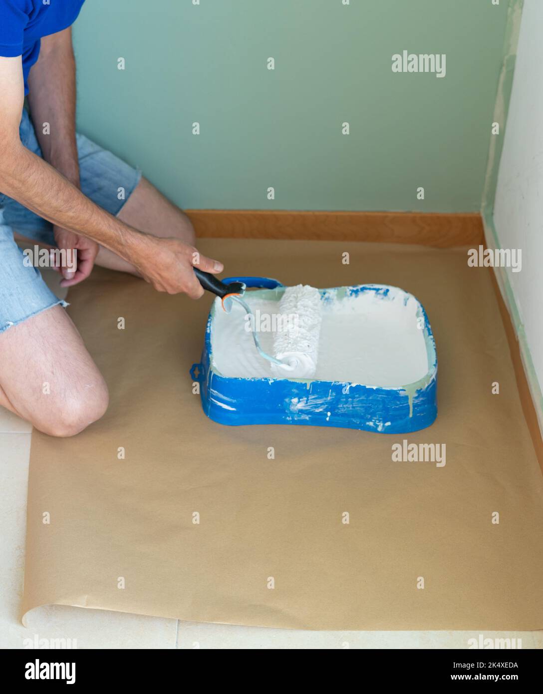 Kneeling man with roller and paint painting the wall. Painter's bucket and roller. Copy space. Stock Photo