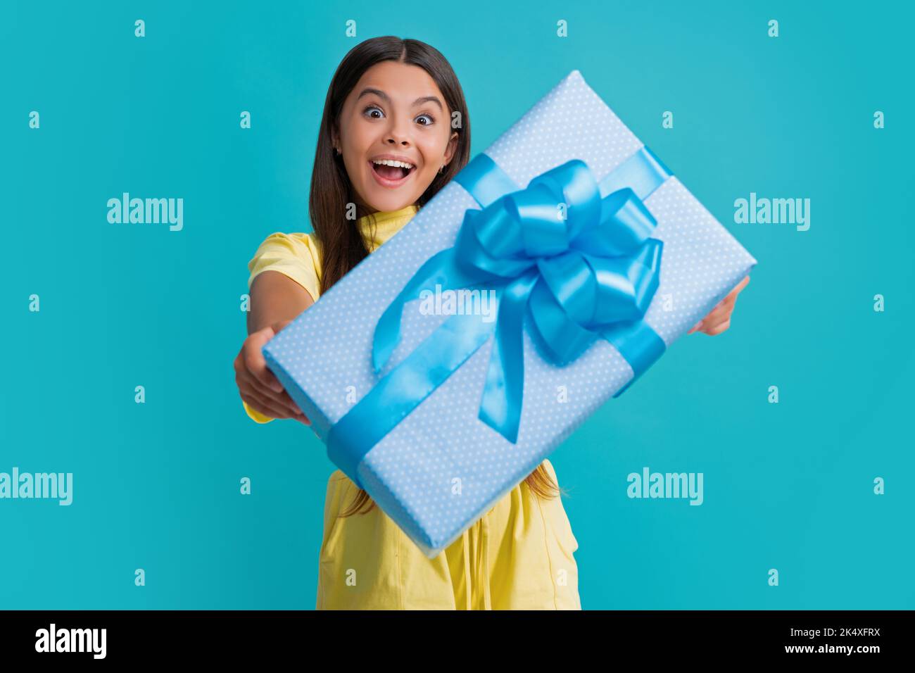 Teenage kid with present box. Teen girl giving birthday gift. Present, greeting and gifting concept. Excited face, cheerful emotions of teenager child Stock Photo